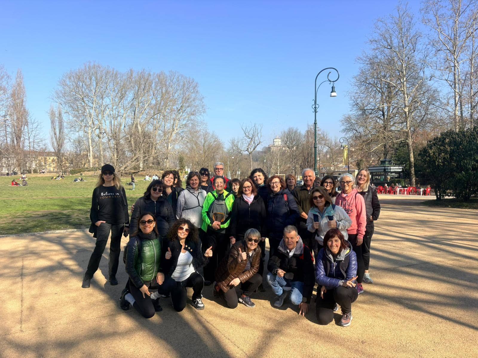 Un grande gruppo di camminatori sorridenti in un parco di Torino in una giornata di sole